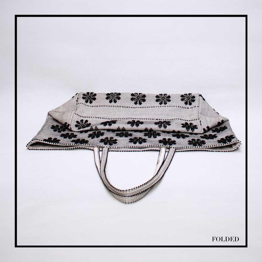 Folded view of a black and white tote bag with a daisies pattern. Main view of our Sustainable tote - summer bag - luxury handbag - handwoven made in Italy by hand - timeless individualistic fashion • eco-friendly fashion • socially responsible, lasting fashion.