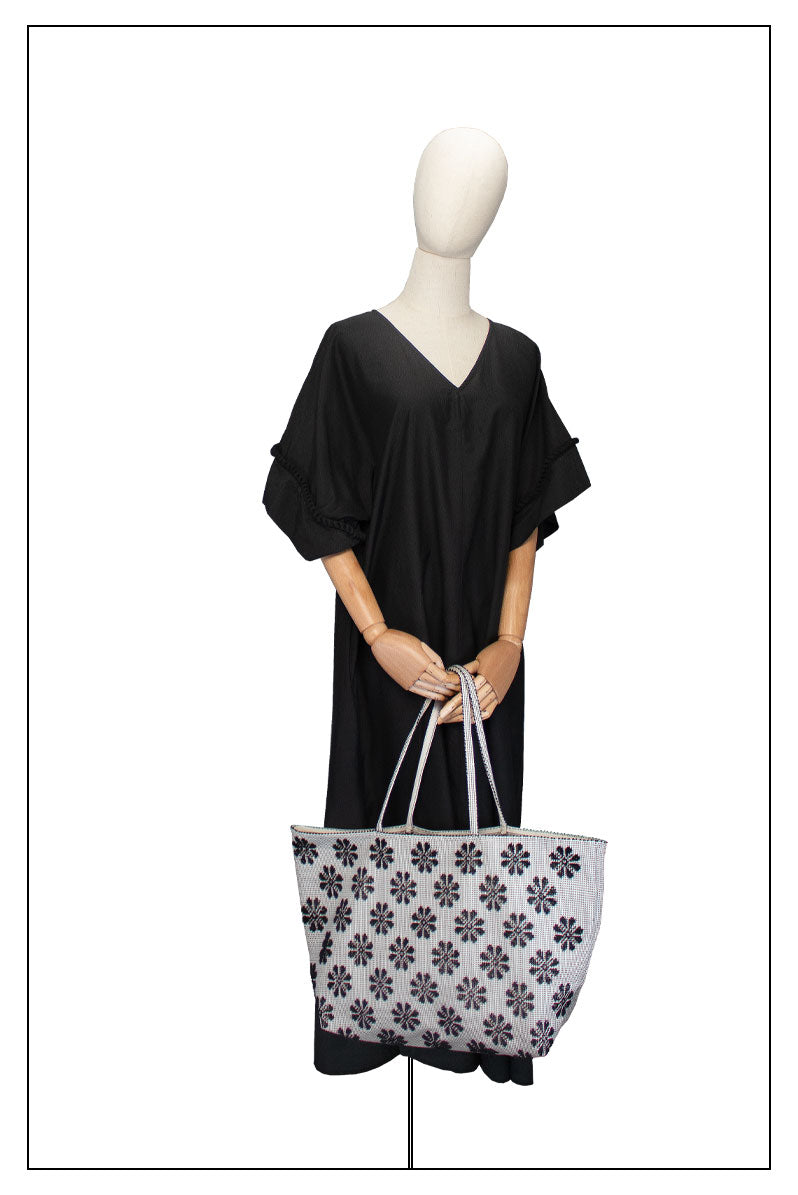 On model view of a black and white tote bag with a daisies pattern. Main view of our Sustainable tote - summer bag - luxury handbag - handwoven made in Italy by hand - timeless individualistic fashion • eco-friendly fashion • socially responsible, lasting fashion.