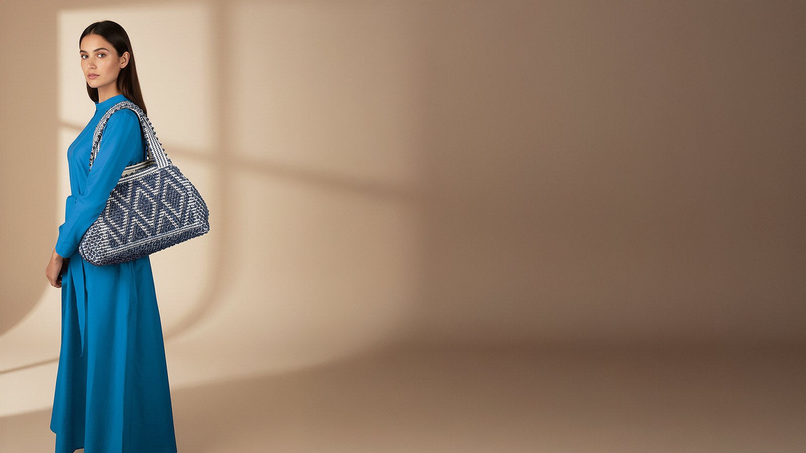 Woman holding a patterned handbag against a beige background - Antonello Tedde entirely hand-woven fabric medium tote bag with diamond pattern with blue melange yarn on white background - handmade in Sardinia, Italy