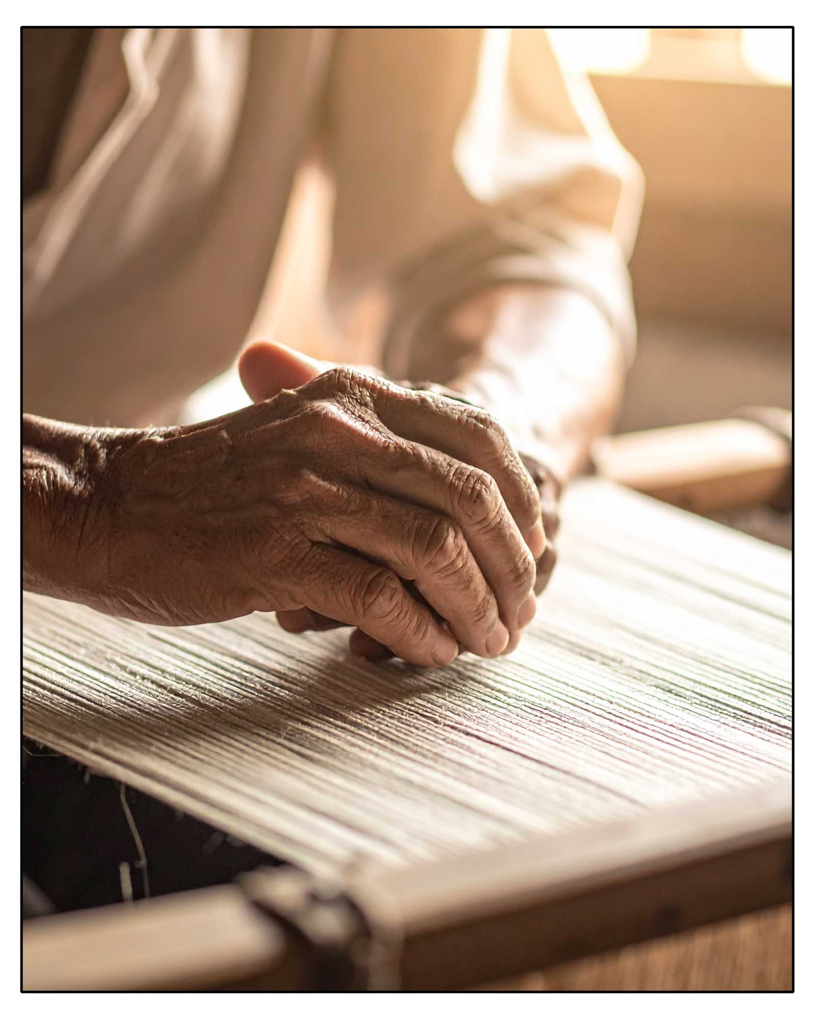 Close-up of an elderly person's hands on a woven mat with a blurred background. This is how the Antonello Tedde Capriccioli Medium Tote Bag is made, handwoven in Sardinia with fuchsia and grey jacquard pattern, yellow handles, and lined interior with pockets on a white background