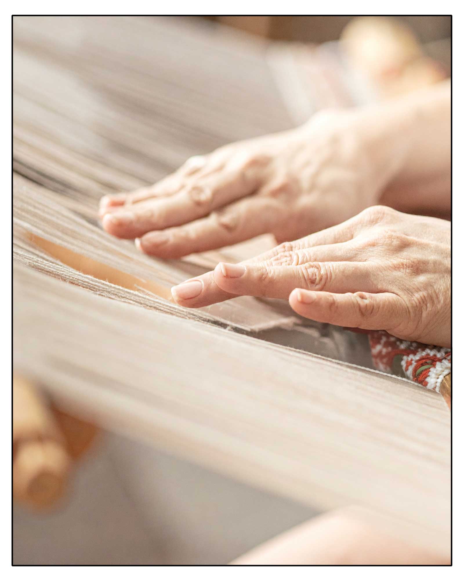 Close-up of an elderly person's hands on a woven fabric with a blurred background. This is how the Antonello Tedde Capriccioli Medium Tote Bag is made, handwoven in Sardinia with fuchsia and grey jacquard pattern, yellow handles, and lined interior with pockets on a white background