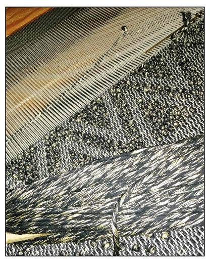 Close-up of a textured fabric with a black, gold, and beige pattern of the Antonello Tedde Pula Medium Tote Bag, handwoven in Sardinia with black and golden yarn, a diamond pattern, and a practical flap pocket