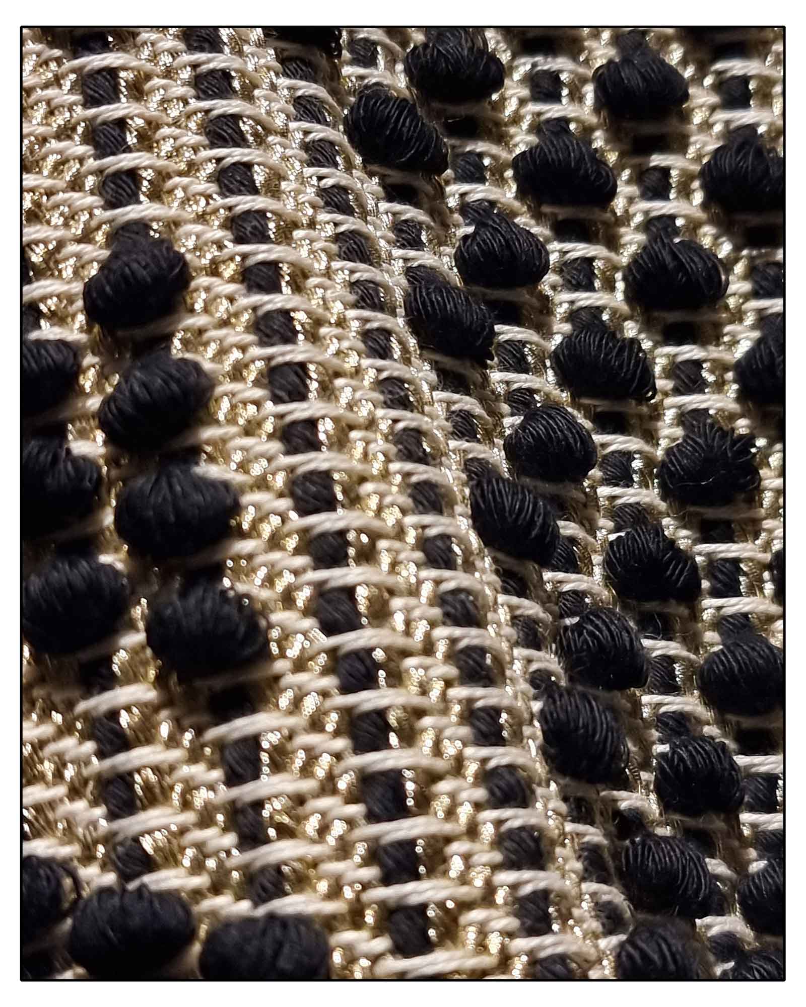 Close-up of a textured fabric with a black, gold, and beige pattern on the Antonello Tedde Pula Medium Tote Bag, handwoven in Sardinia with black and golden yarn, a diamond pattern, and a practical flap pocket. 