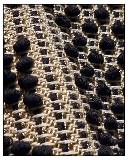 Close-up of a textured fabric with a black, gold, and beige pattern on the Antonello Tedde Pula Medium Tote Bag, handwoven in Sardinia with black and golden yarn, a diamond pattern, and a practical flap pocket. 