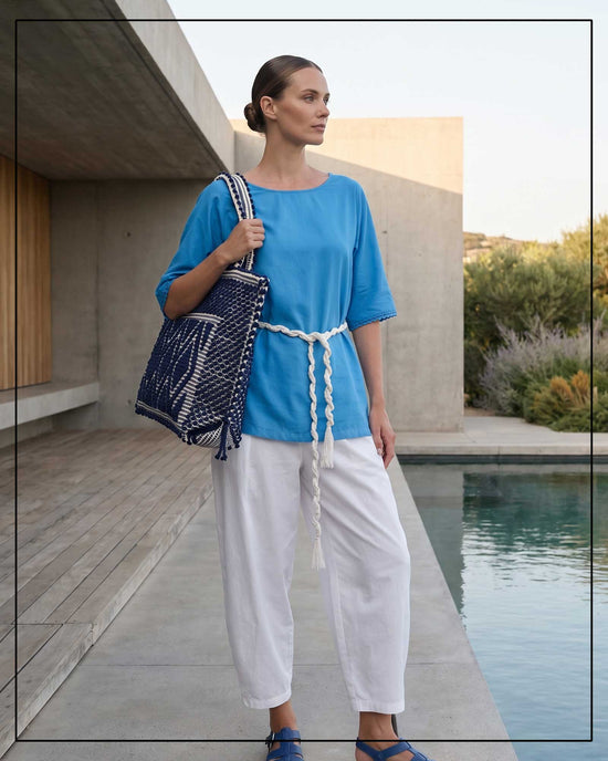 A woman in a blue top and white pants holding a blue and white bag by a poolside. All by Antonello Tedde