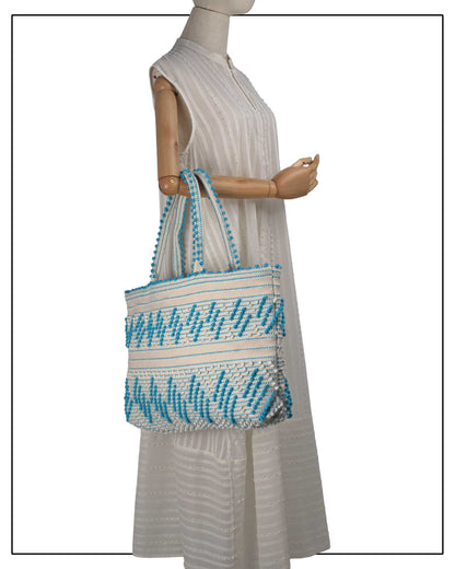 Mannequin wearing a light-coloured dress with Antonello Tedde Mugoni Zig Zag Tote Bag, handwoven in Sardinia from linen and cotton with geometric zig zag weave and diamond motifs - Front view of tote bag with turquoise on a cream background