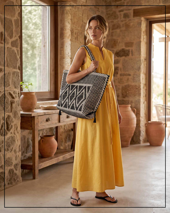 Woman in a yellow dress holding a patterned bag in a rustic interior setting. Black and white handwoven handbag with a geometric pattern on a white background by Antonello Tedde 