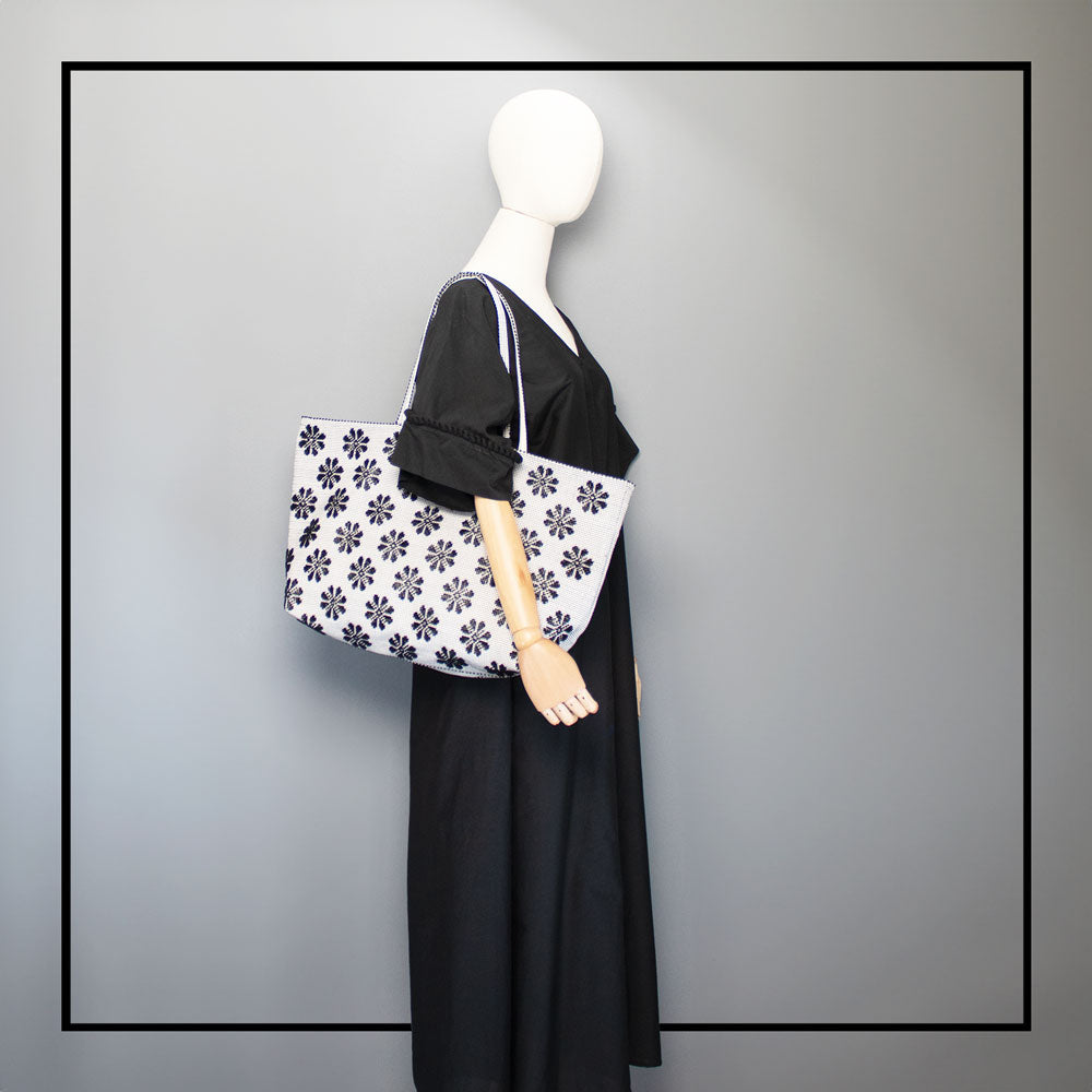 on model view of a black and white tote bag with a daisies pattern.  Here warned on shoulder with a black dress - Main view of our Sustainable tote - summer bag - luxury handbag - handwoven made in Italy by hand  - timeless individualistic fashion • eco-friendly fashion • socially responsible, lasting fashion.