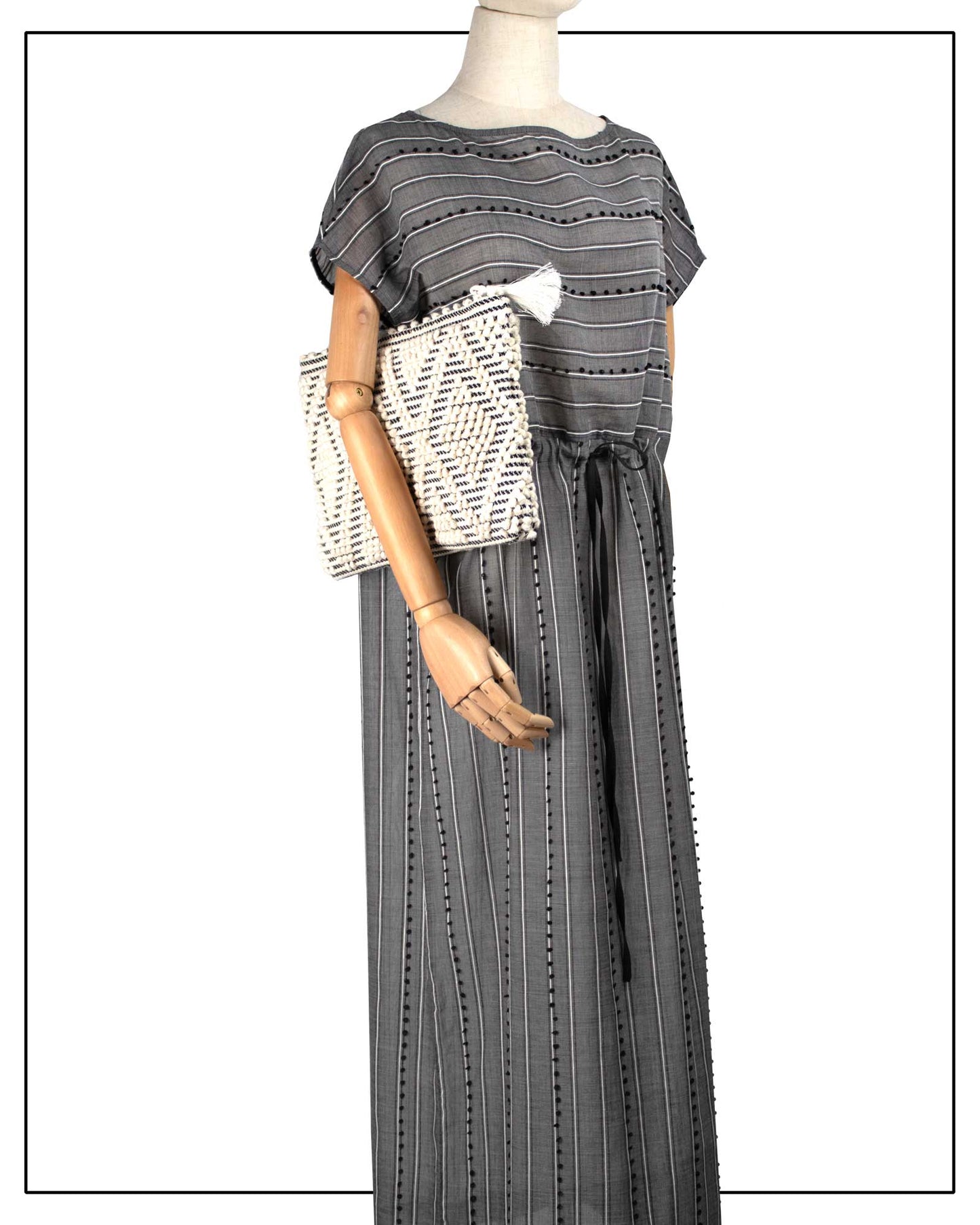 Mannequin wearing a grey striped dress with a white Antonello Tedde Hand-woven clutch bag with black and white pattern on a white background