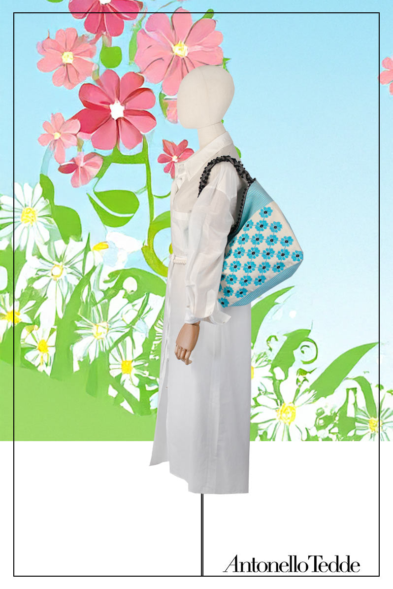 Mannequin wearing a white outfit with a colourful bag against a floral background. view of a turquoise, black and white tote bag with a daisy pattern. Main view of our Sustainable tote - summer bag - luxury handbag - handwoven made in Italy by hand  - timeless individualistic fashion • eco-friendly fashion • socially responsible, lasting fashion.
