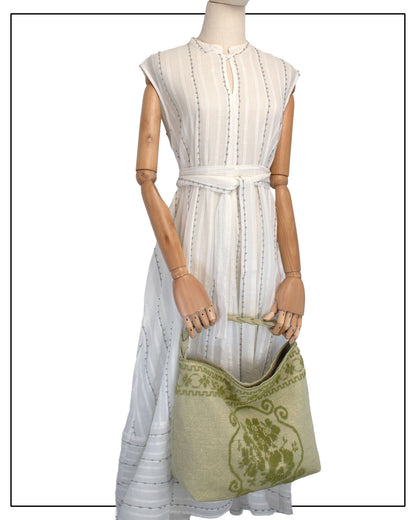 Antonello Tedde Banari Tote Bag handwoven in Sardinia using the traditional small Pibiones technique with green regenerated cotton, golden yarn, and floral bouquet motif. On the model view held with both hands