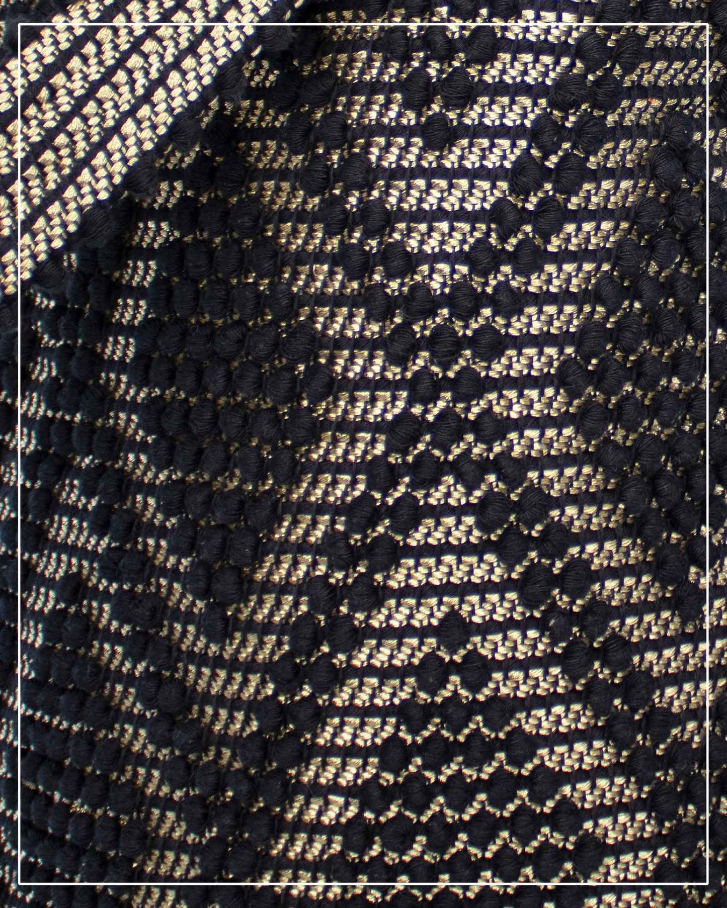 A close-up of a woven textile pattern featuring an Antonello Tedde Bultei Rombi tote bag, handwoven in Sardinia from black cotton with a shimmering golden viscose diamond pattern. 