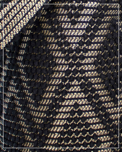A close-up of a woven textile pattern featuring an Antonello Tedde Bultei Rombi tote bag, handwoven in Sardinia from black cotton with a shimmering golden viscose diamond pattern. 