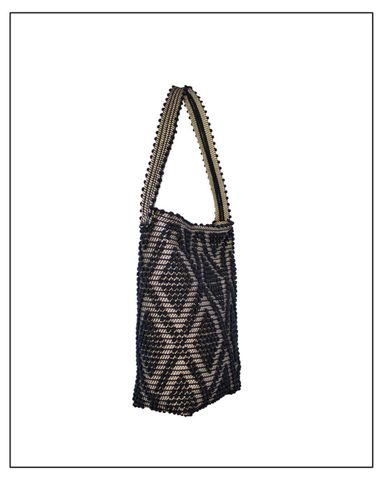 Side view of an Antonello Tedde Bultei Rombi shoulder bucket bag, handwoven in Sardinia from black cotton with a shimmering golden viscose diamond pattern. 