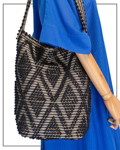 Detail of a close-up of a mannequin wearing a bright royal blue maxi dress with short, wide sleeves and a V-neckline, styled with an Antonello Tedde Bultei Rombi tote bag, handwoven in Sardinia from black cotton with a shimmering golden viscose diamond pattern. 