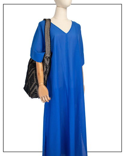 A mannequin wearing a bright royal blue maxi dress with short, wide sleeves and a V-neckline, styled with an Antonello Tedde Bultei Rombi tote bag, handwoven in Sardinia from black cotton with a shimmering golden viscose diamond pattern.