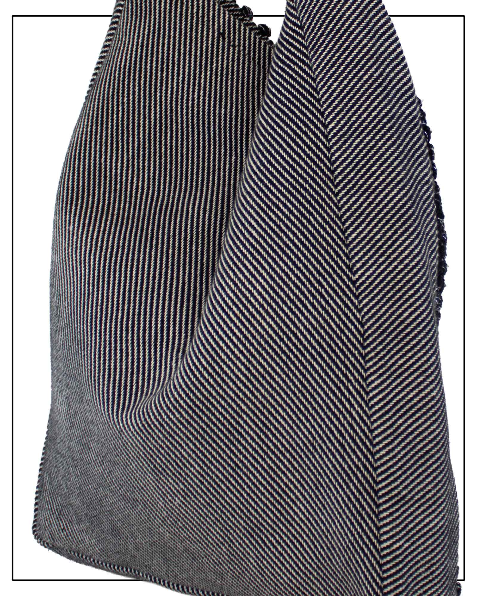 A close-up of the back view of Antonello Tedde Bultei's handwoven tote bag in black cotton with subtle silver highlights and a textured woven front panel, handcrafted in Sardinia. and white herringbone pattern, showing the texture and fold details against a white background.