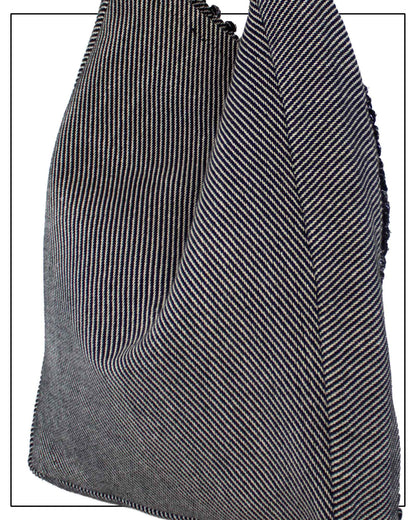 A close-up of the back view of Antonello Tedde Bultei's handwoven tote bag in black cotton with subtle silver highlights and a textured woven front panel, handcrafted in Sardinia. and white herringbone pattern, showing the texture and fold details against a white background.