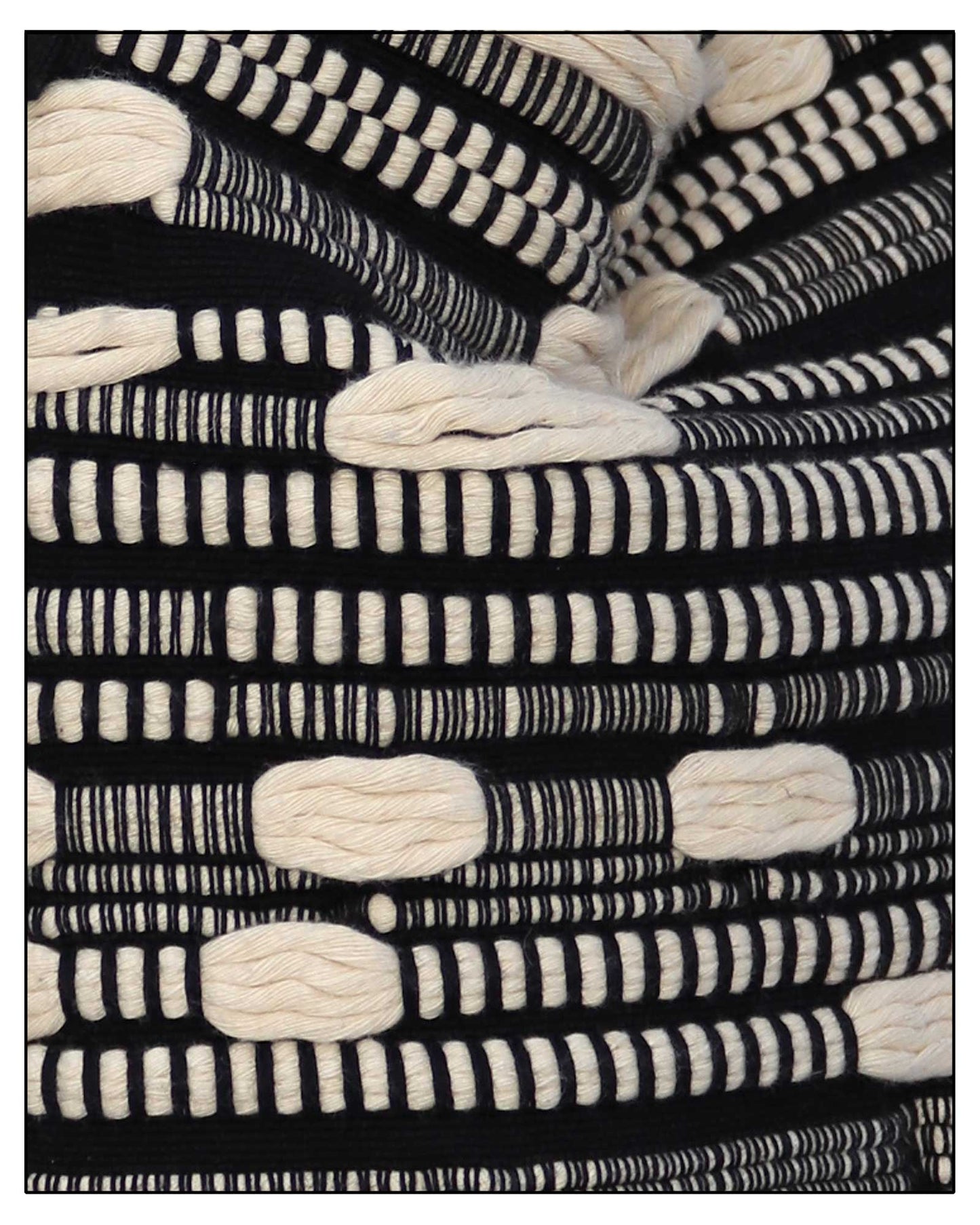 A close-up of a woven textile with a bold black and off-white geometric pattern, featuring thick textured loops and horizontal striped bands. Fabric view of Antonello Tedde Bultei Tote Bag from the Trame in Fuga Collection, handwoven in Sardinia with black and natural cotton, textured woven motifs, and artisanal craftsmanship.
