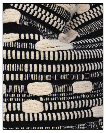A close-up of a woven textile with a bold black and off-white geometric pattern, featuring thick textured loops and horizontal striped bands. Fabric view of Antonello Tedde Bultei Tote Bag from the Trame in Fuga Collection, handwoven in Sardinia with black and natural cotton, textured woven motifs, and artisanal craftsmanship.