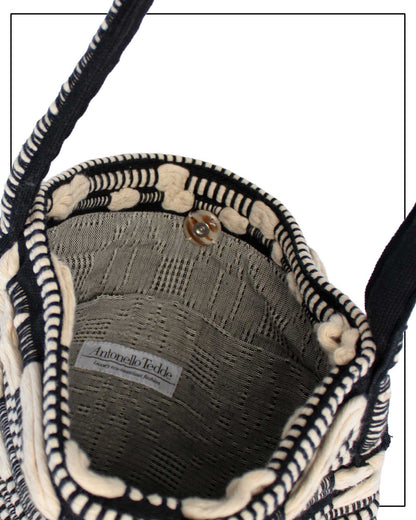 Close-up of the interior of a woven handbag, showing a black and off-white striped woven body, a grey patterned lining, and a white brand label reading  Antonello Tedde. Bultei Tote Bag from the Trame in Fuga Collection, handwoven in Sardinia with black and natural cotton, textured woven motifs, and artisanal craftsmanship.