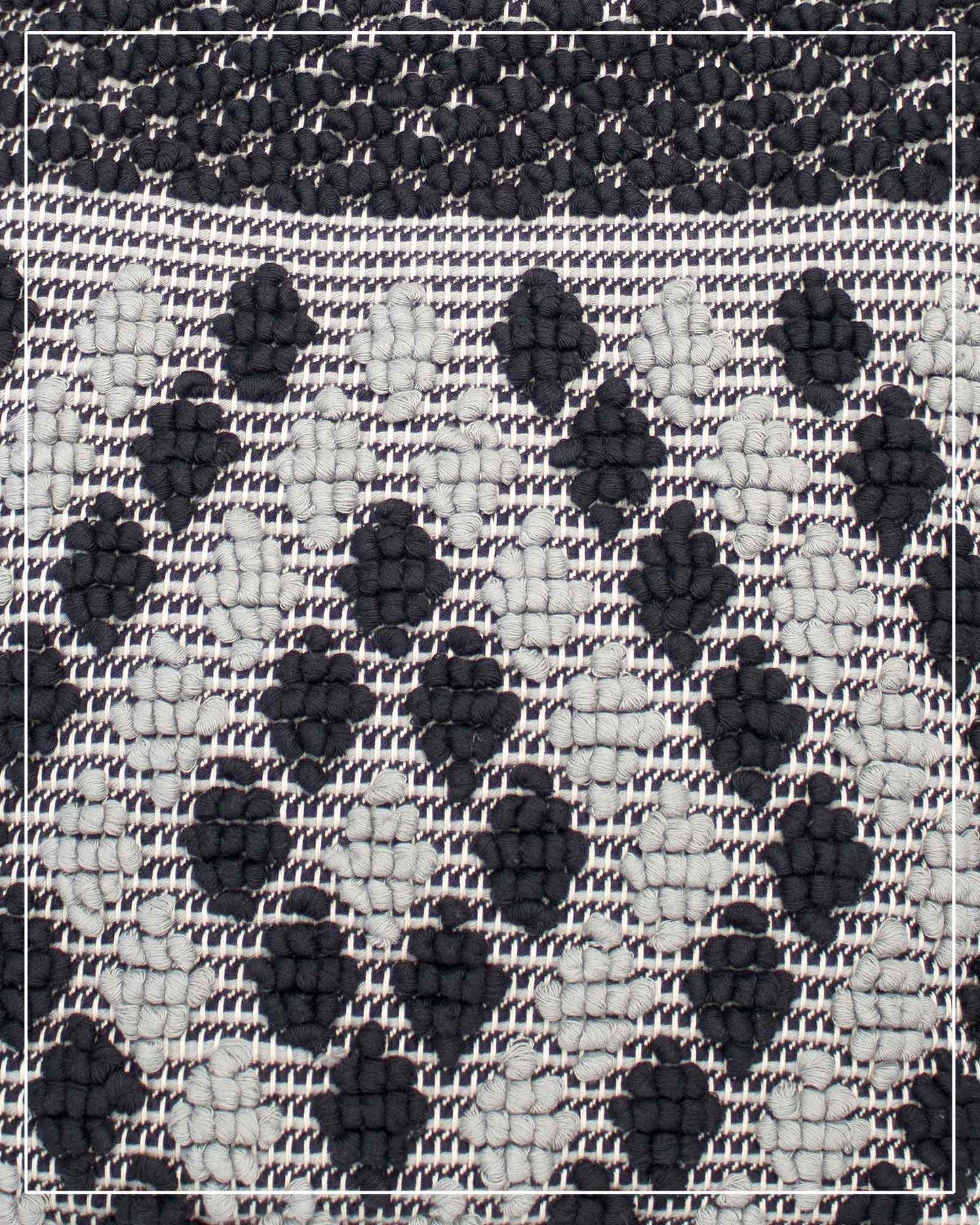 A close-up of a woven textile pattern featuring a black and off-white checkered base with raised black diamond-like motifs. Antonello Tedde Capriccioli Large handwoven cotton tote bag in black and grey with Rombetti small diamond pattern.