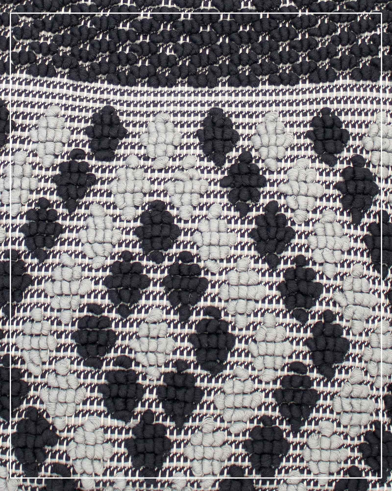 A close-up of a woven textile pattern featuring a black and off-white checkered base with raised black diamond-like motifs. Antonello Tedde Capriccioli Large handwoven cotton tote bag in black and grey with Rombetti small diamond pattern.