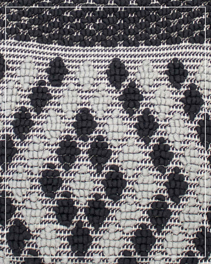 A close-up of a woven textile pattern featuring a black and off-white checkered base with raised black diamond-like motifs. Antonello Tedde Capriccioli Large handwoven cotton tote bag in black and grey with Rombetti small diamond pattern.