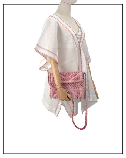 A pink woven clutch bag with a matching braided shoulder strap is displayed on a mannequin wearing a white embroidered caftan. The mannequin is set against a plain white background.