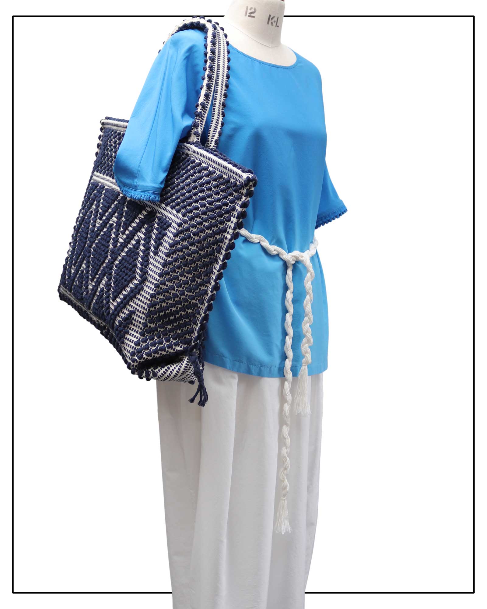 Mannequin wearing a blue top and white pants with a dark blue woven bag. Main view front handbag capriccioli  - Sustainable tote - summer bag - luxury handbag - handwoven BLUE with CREAM base tote made in Italy by hand • timeless individualistic fashion • eco-friendly fashion • socially responsible, lasting fashion.