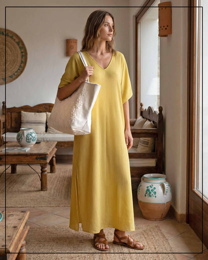 A woman in a yellow dress holding a beige tote bag in a rustic interior setting. Raised flower pattern handwoven cream tote bag, all by Antonello Tedde.