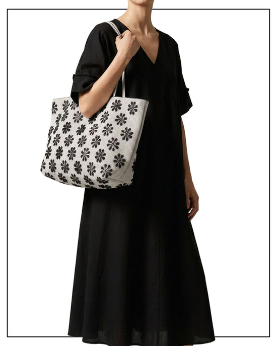 Mannequin wearing a black dress holding a grey tote bag with a floral pattern on a white background. Front view of a black and white tote bag with a daisy pattern. Main view of our Sustainable tote - summer bag