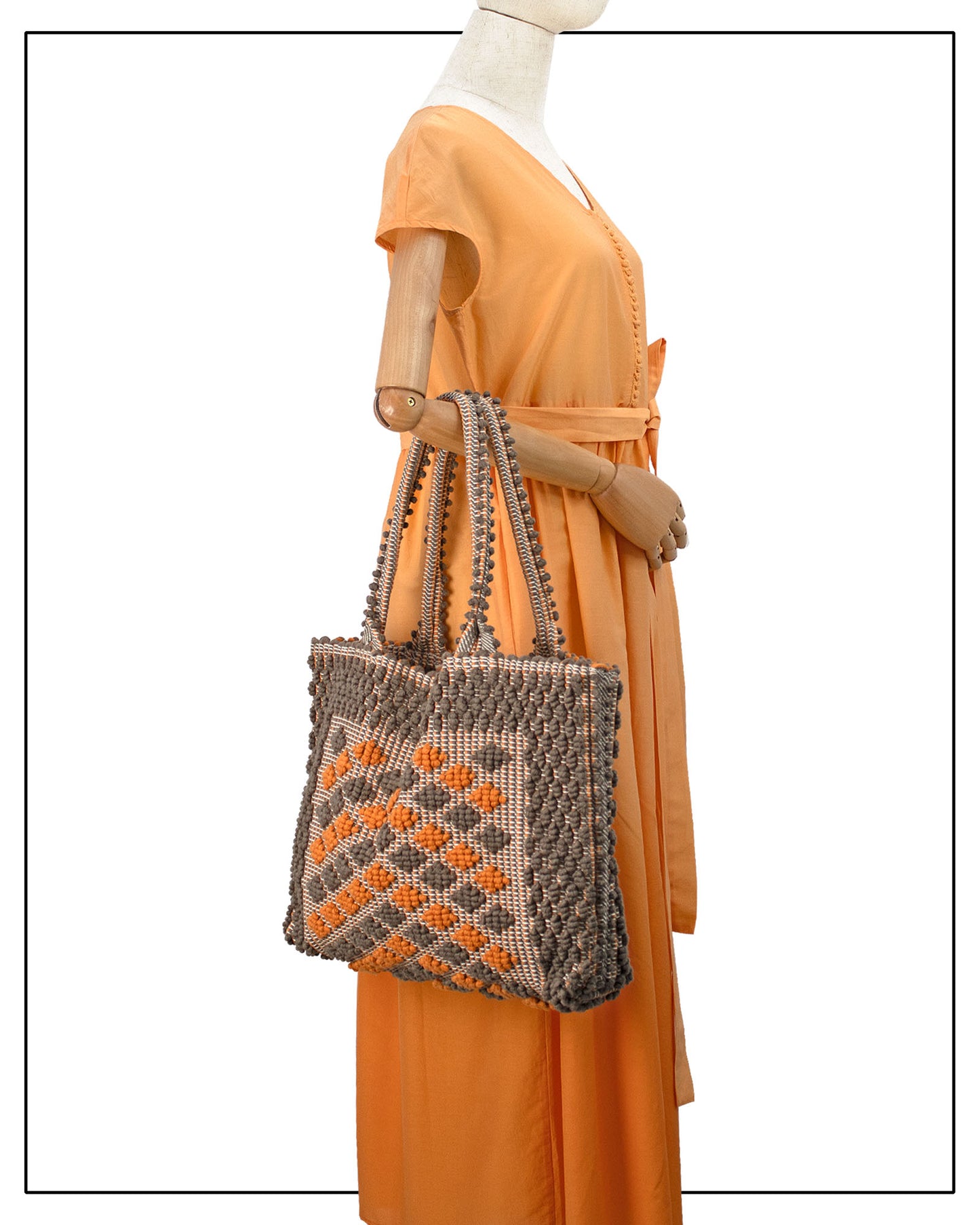 Mannequin wearing an orange dress with a medium-sized, ethically crafted Sardinian handwoven cotton tote bag with taupe and orange colors, featuring a geometric rombetti pattern. 