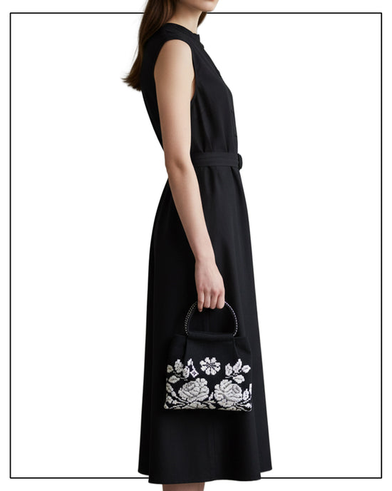 Woman wearing a black sleeveless dress holding a floral embroidered handbag on a white background by Antonello Tedde