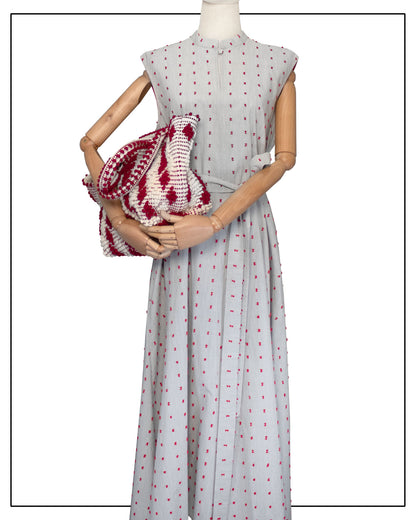 Mannequin wearing an Antonello Tedde long light grey dress with red patterns, holding a matching red-and-white patterned bag. Red-and-white patterned handbag on a white background. Celvia Medium Red and Cream Tote Bag is handwoven, a reimagined classic that marks the return of the beloved rombetti (Multiple Diamonds) pattern in a fresh, contemporary silhouette