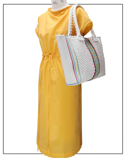 Yellow dress with a white bag featuring colourful stripes on a plain background, Antonello Tedde Urtei Medium Tote Bag, handwoven in Sardinia with cream cotton, multicoloured stripe. 