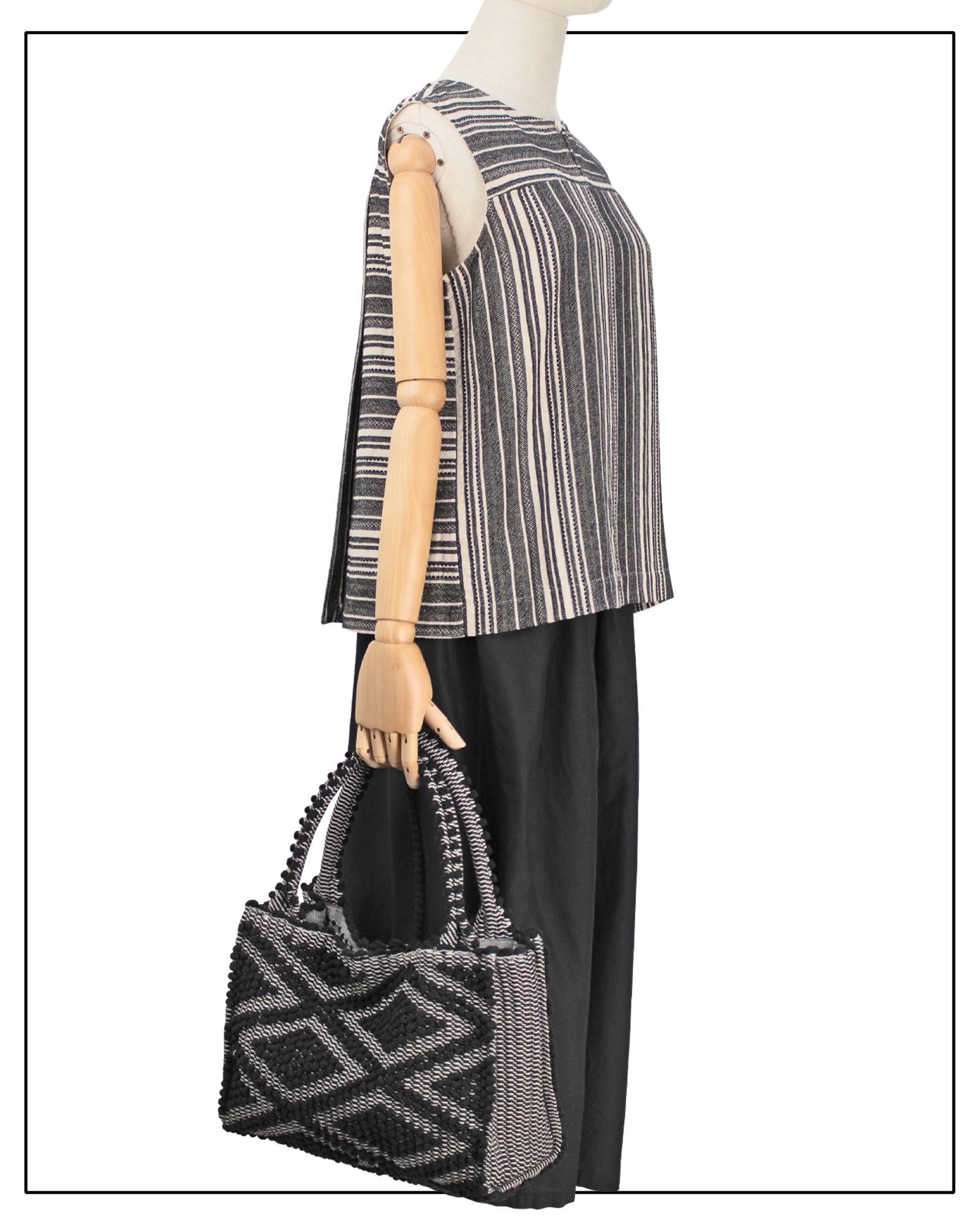 Mannequin wearing a striped top and black pants holding a patterned - Main front view for HOBO BLACK IN BLACK WITH BLACK BASE. The best eco luxury bags and accessories brand. Stylish clothes and an Eco-Friendly handbag with recycled yarn.