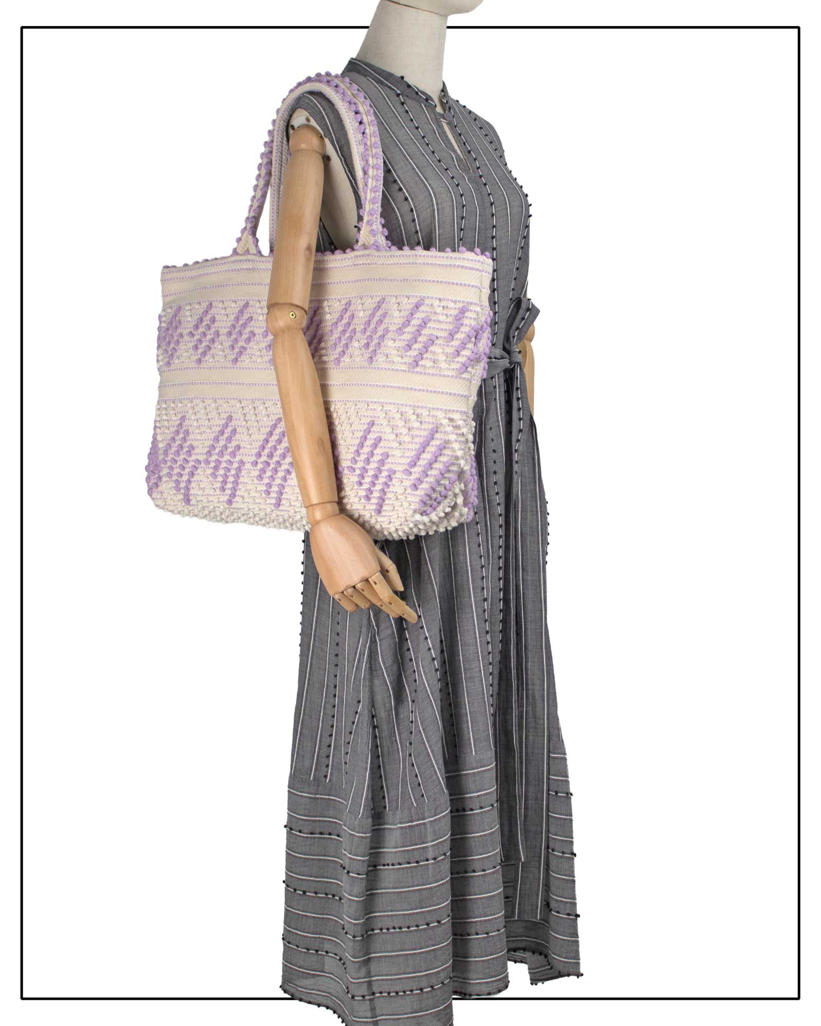 Mannequin wearing a grey dress with a purple-and-white patterned bag. Antonello Tedde Mugoni Zig Zag Tote Bag, handwoven in Sardinia from linen and cotton with geometric zig zag weave and diamond motifs.