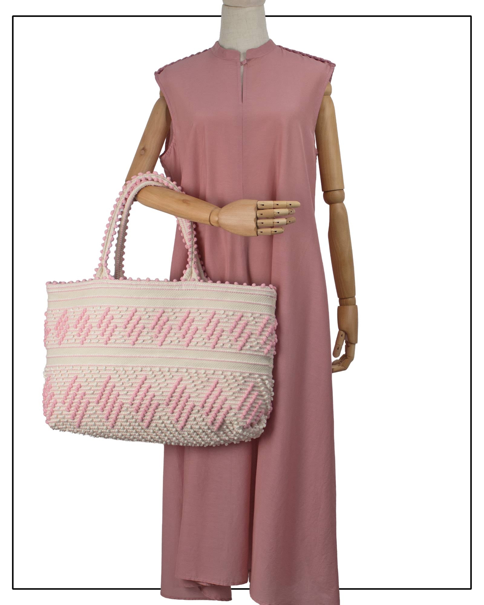 Mannequin wearing a pink dress, holding a pink-and-white woven bag. Antonello Tedde Mugoni Zig Zag Tote Bag, handwoven in Sardinia from linen and cotton with geometric zig zag weave and diamond motifs -  frontal view of tote bag with pink on a cream background