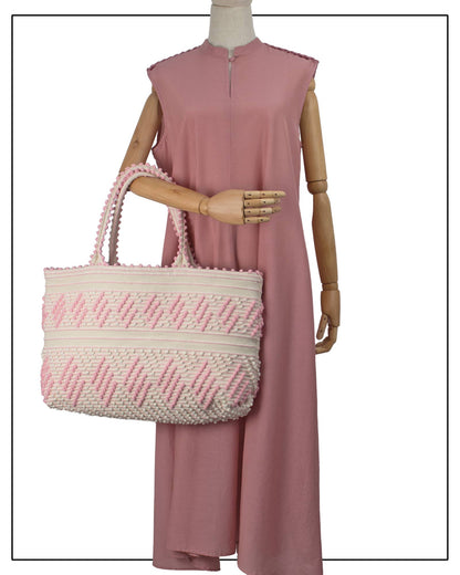 Mannequin wearing a pink dress, holding a pink-and-white woven bag. Antonello Tedde Mugoni Zig Zag Tote Bag, handwoven in Sardinia from linen and cotton with geometric zig zag weave and diamond motifs -  frontal view of tote bag with pink on a cream background