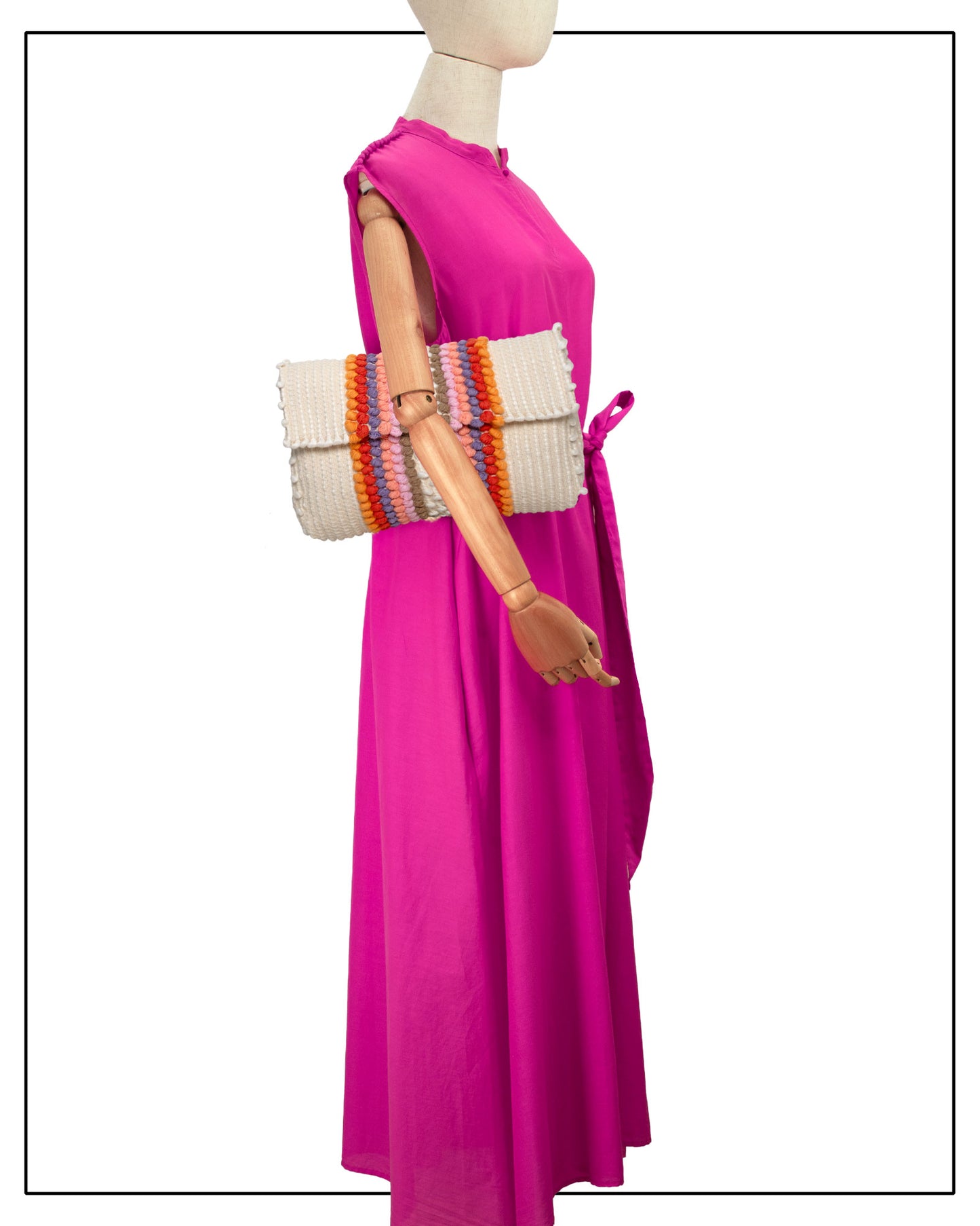 A sleeveless magenta-pink maxi dress displayed on a mannequin, styled with a Antonello Tedde Suni Fire crossbody bag handwoven in Sardinia in cream linen and cotton with colourful raised stripes and braided shoulder strap