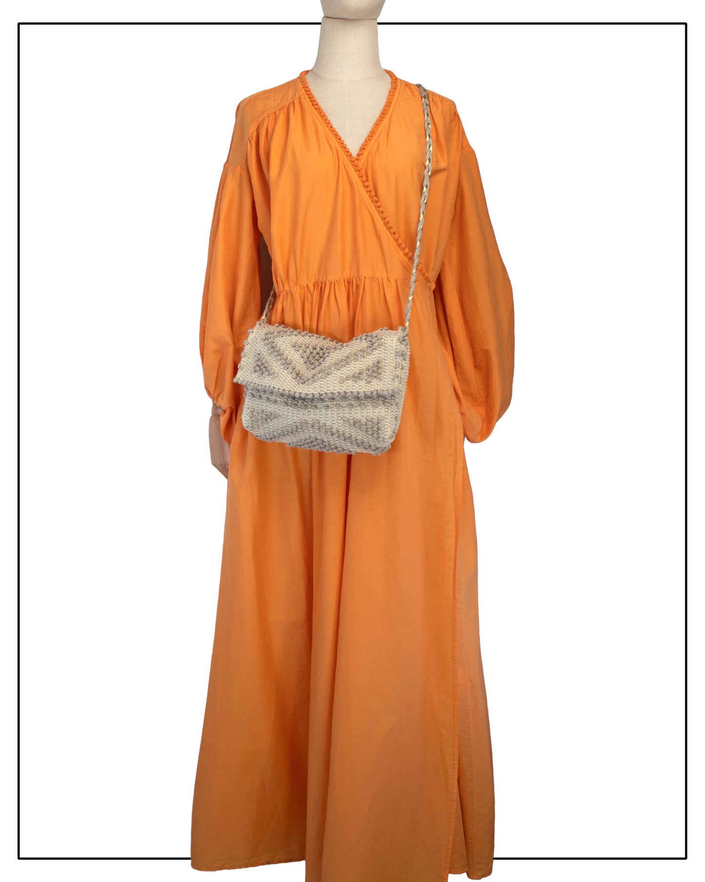 An orange long-sleeve maxi dress displayed on a mannequin, styled with an Antonello Tedde Suni Square crossbody bag, handwoven in Sardinia from natural cord linen with a subtle golden yarn and a braided shoulder strap.