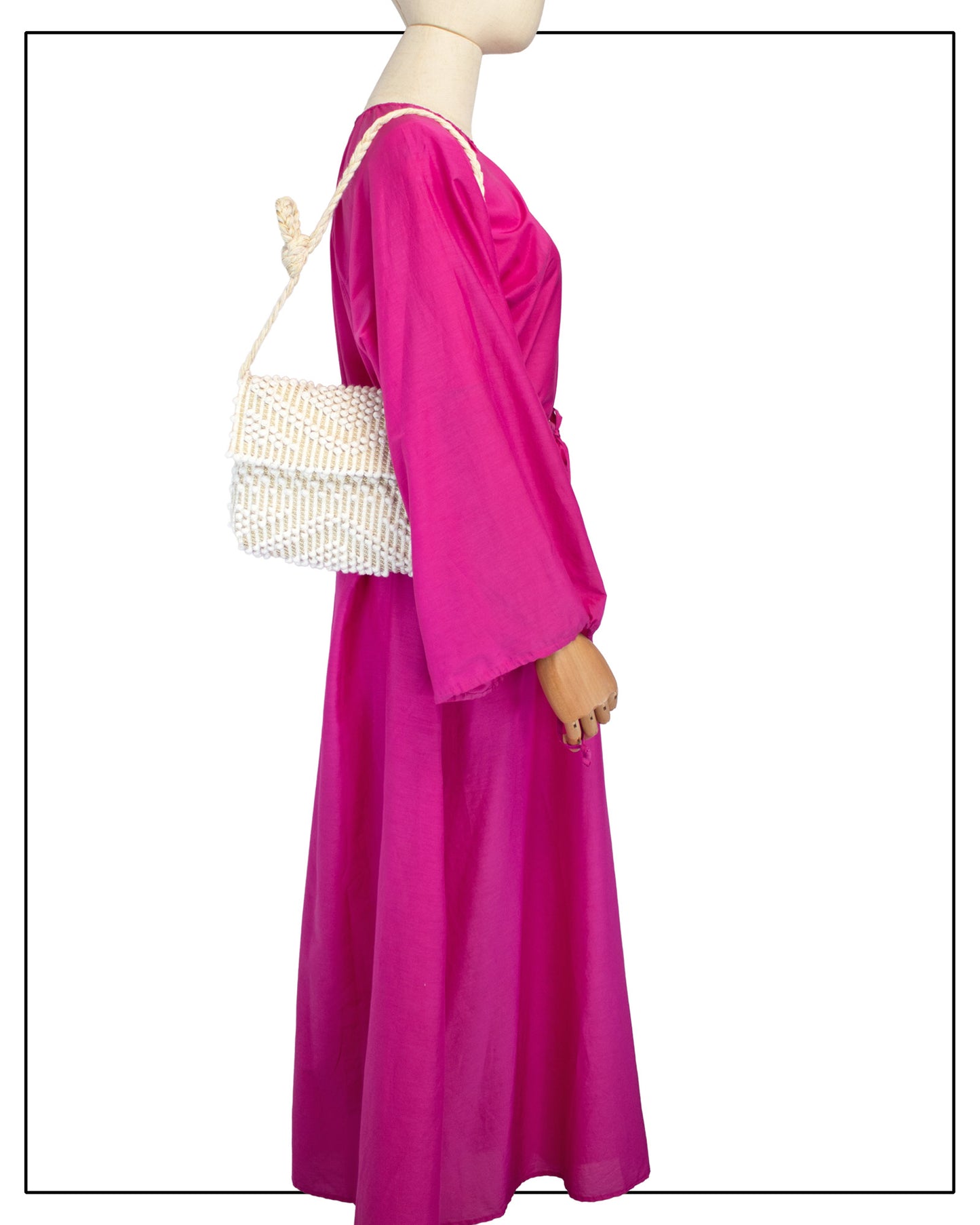 A mannequin wearing a bright fuchsia maxi dress with wide sleeves, shown from the side. Styled with an Antonello Tedde Suni Small crossbody bag, handwoven in Sardinia in cream Italian linen, ivory and subtle golden yarn with a braided strap.