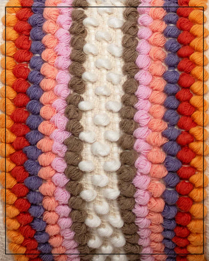 View of Antonello Tedde Suni Fire crossbody bag fabric, handwoven in Sardinia in cream linen and cotton with colourful raised stripes and braided shoulder strap.A close-up of a colourful knitted textile with vertical stripes of textured yarn in cream, taupe, pink, peach, purple, red, orange, and yellow.