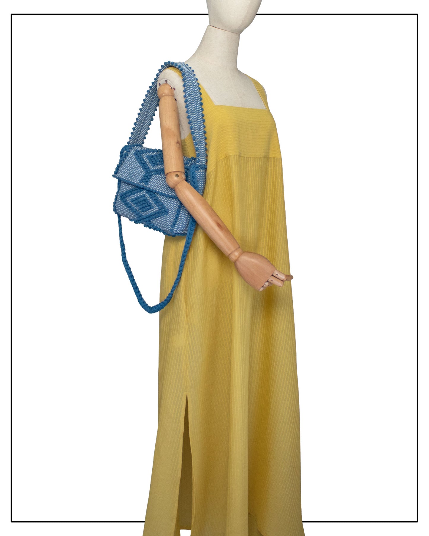 A yellow sleeveless maxi dress displayed on a mannequin, styled with an Antonello Tedde Suni X crossbody bag handwoven in Sardinia from denim blue, grey and cream cotton with raised rombi pattern and braided shoulder strap