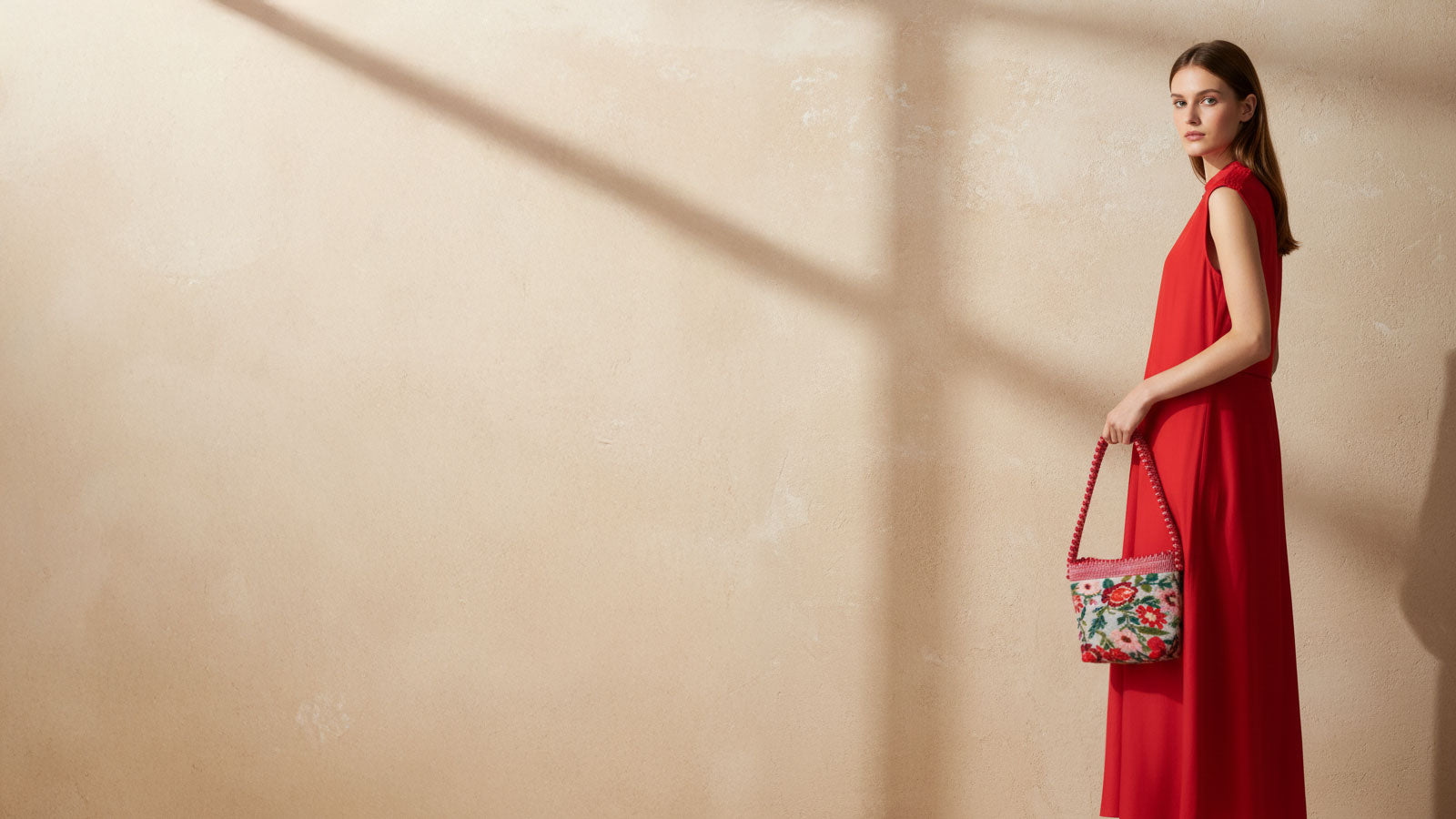 Woman in a red dress holding a floral handbag against a beige wall