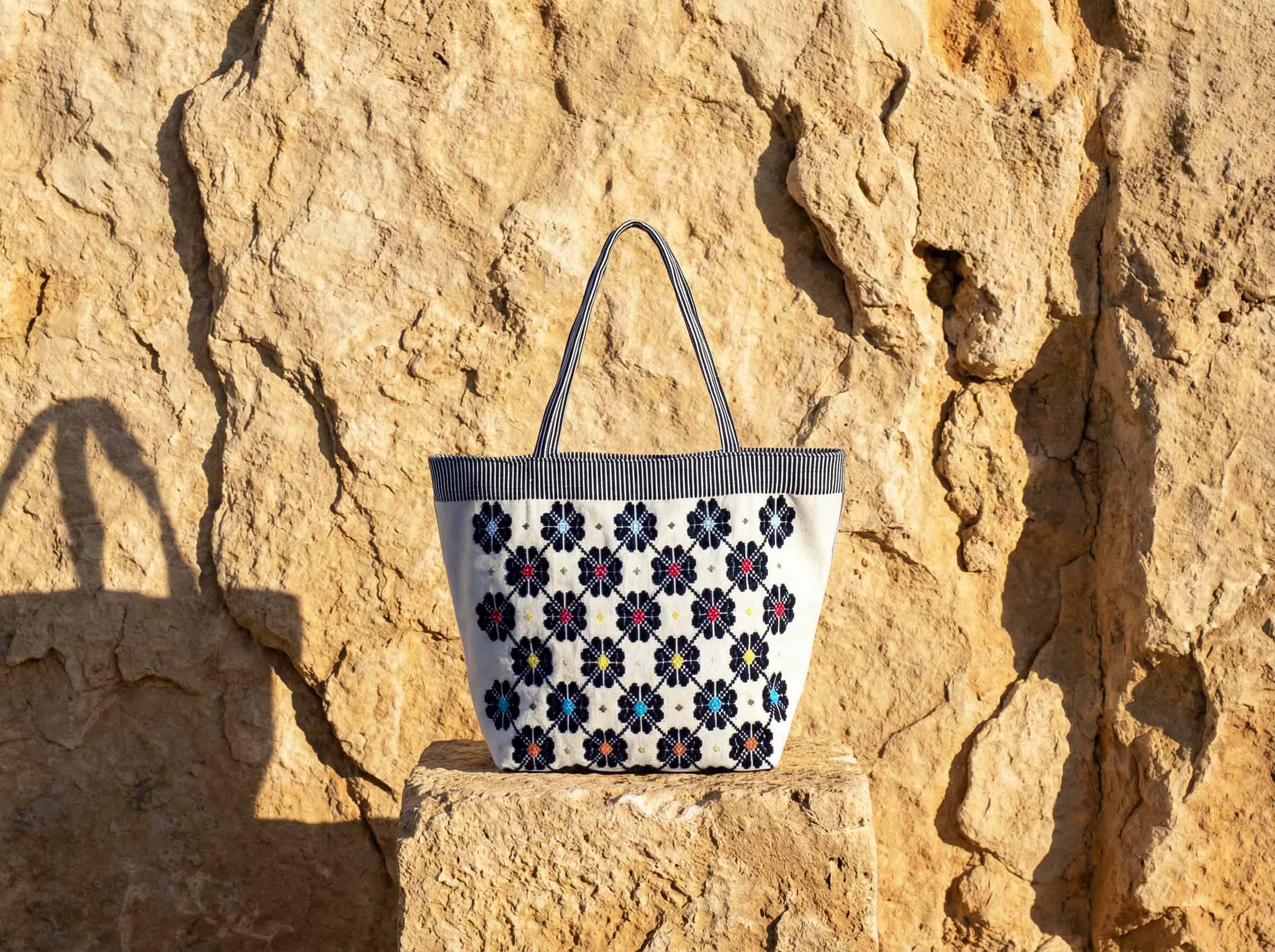 Handwoven sustainable luxury bag by Antonello Tedde displayed against Mediterranean stone wall