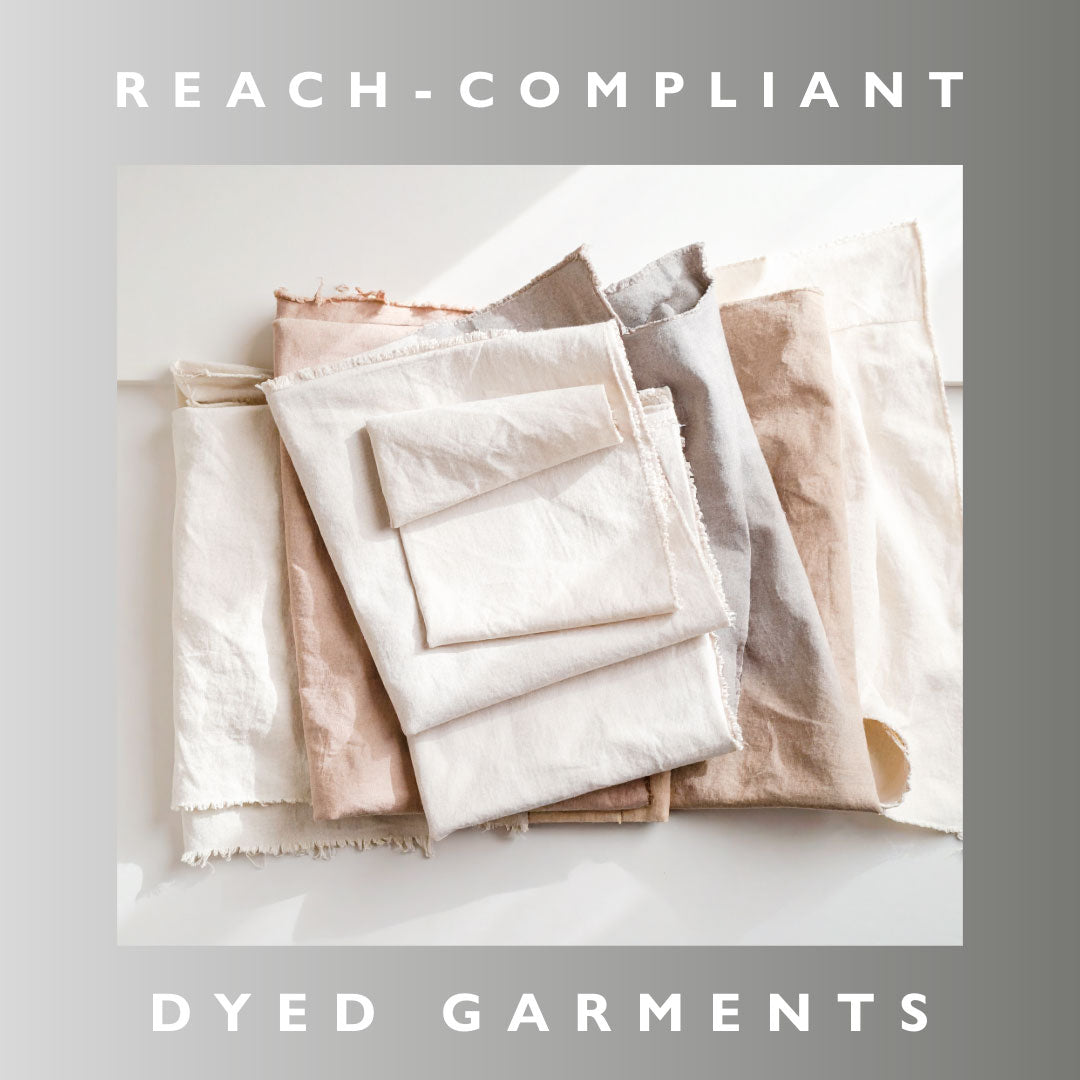 Stack of folded dyed garment fabrics on a light background with 'REACH-COMPLIANT' text above.
