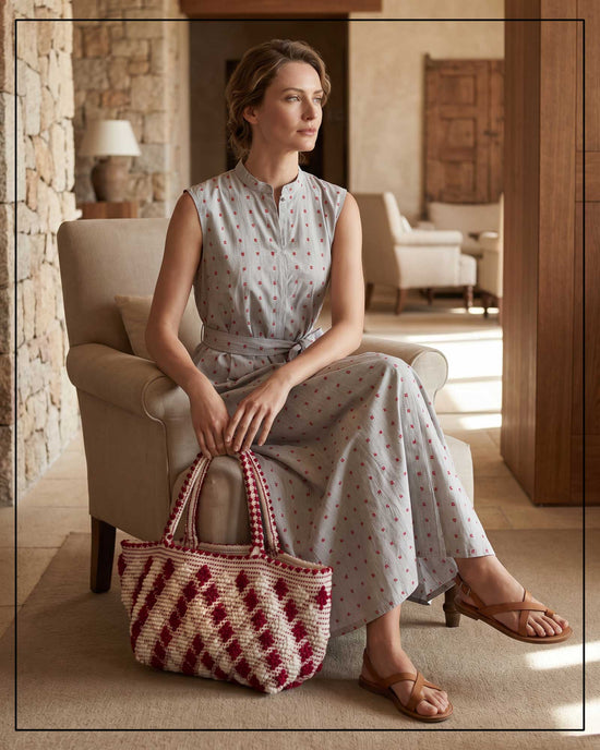 A woman sitting on a chair holding a red and white patterned bag in a sunlit room.